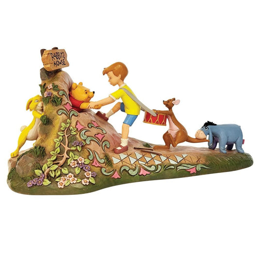 Enesco Jim Shore-beeldje van Christopher Robin, Kanga, Iejoor, Konijn en Pooh die samen het huis van Konijn verlaten, met kenmerkende Jim Shore details en zachte bloemaccenten.
